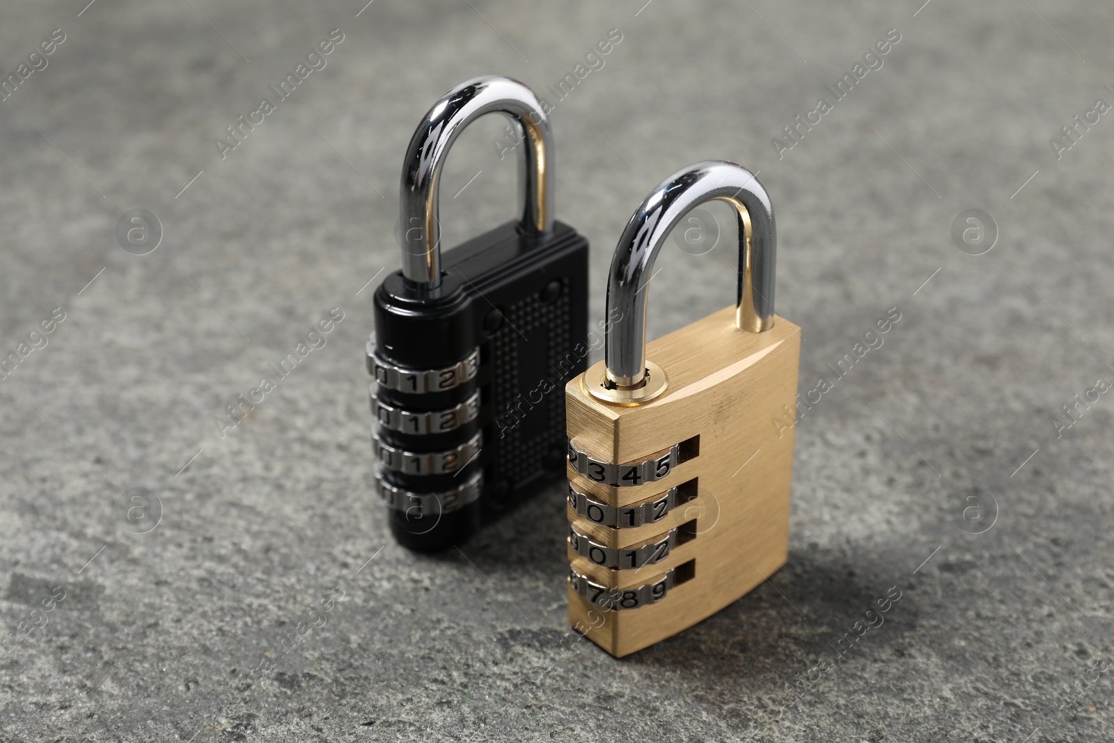 Photo of Locked steel combination padlocks on grey stone table, closeup