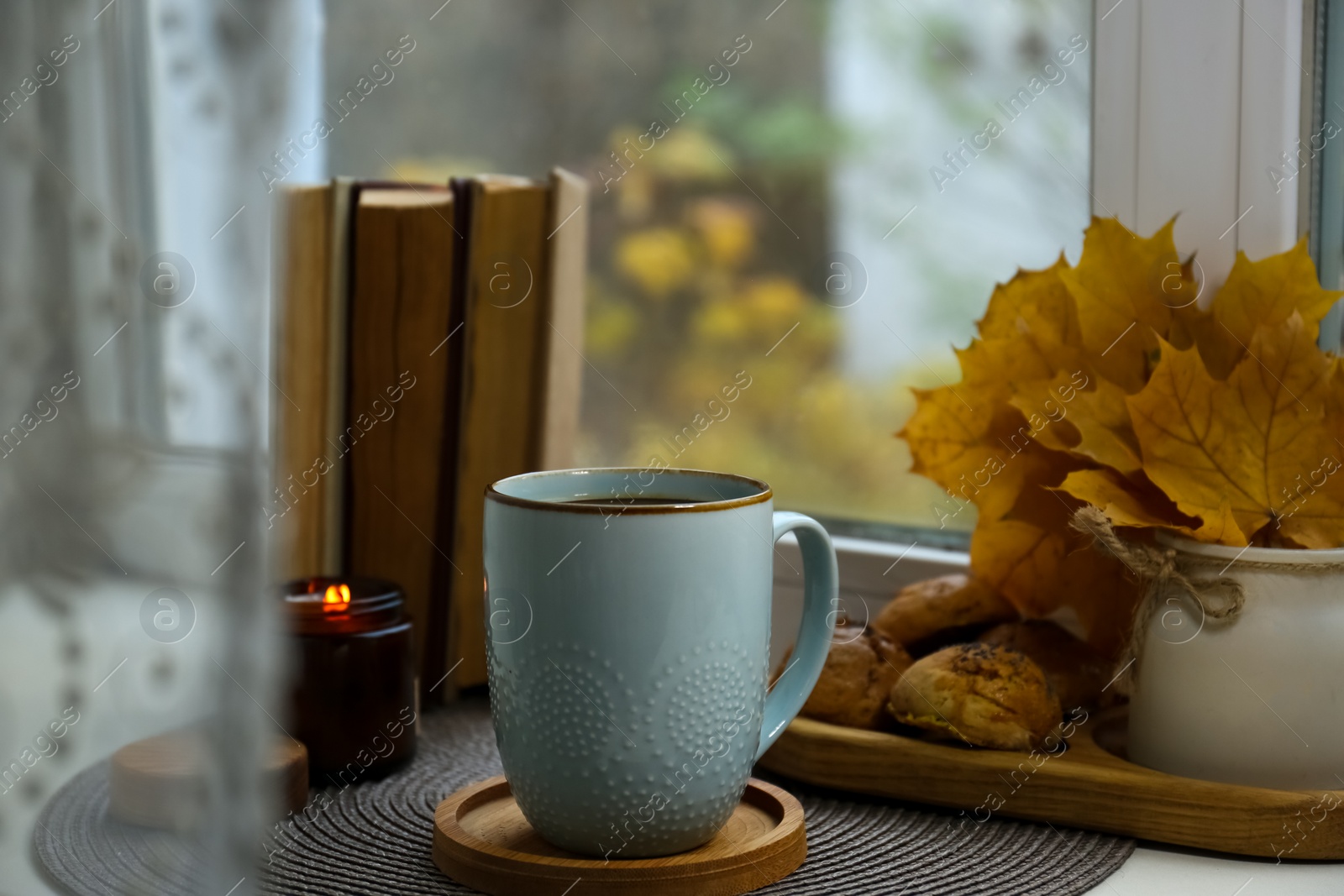 Photo of Cup of tasty hot drink near books, burning candle and cookies on windowsill. Autumn coziness