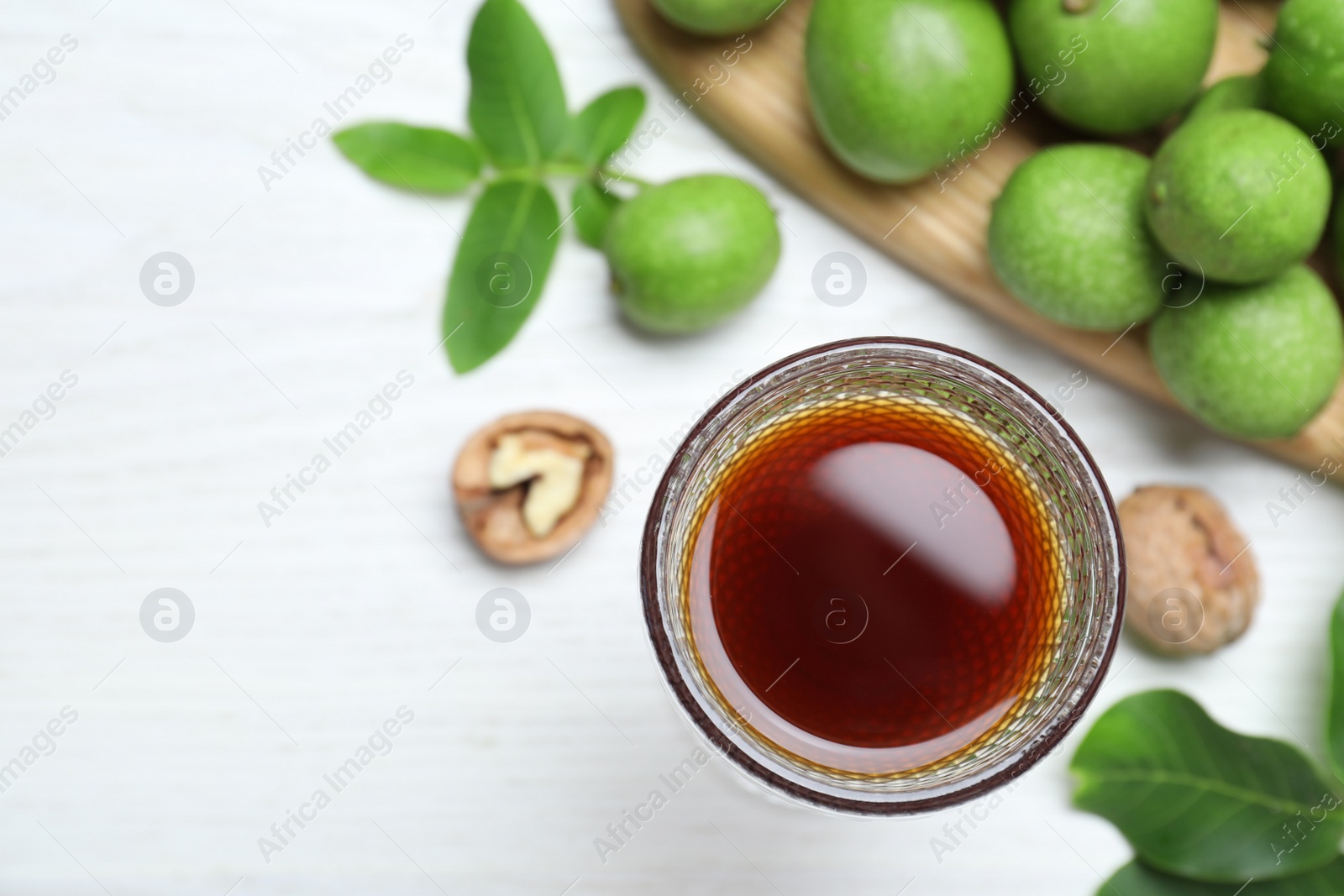 Photo of Delicious liqueur and fresh walnuts on white wooden table, flat lay. Space for text