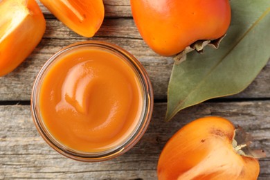 Delicious persimmon jam in glass jar and fresh fruits on wooden table, flat lay