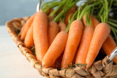 Photo of Wicker tray with ripe carrots on table, closeup