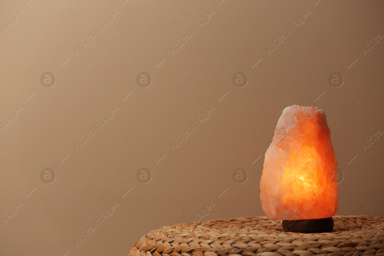 Photo of Himalayan salt lamp on wicker table against beige background. Space for text