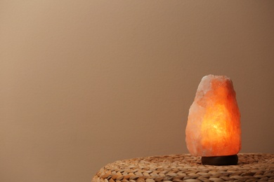 Photo of Himalayan salt lamp on wicker table against beige background. Space for text