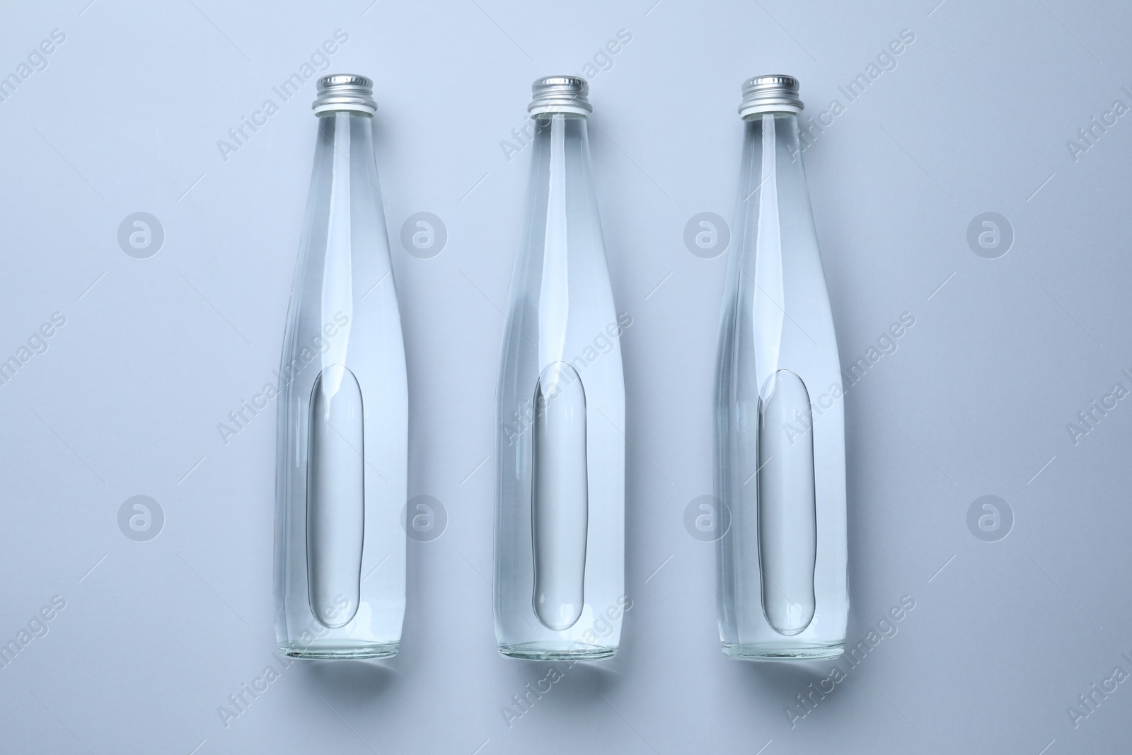 Photo of Glass bottles with water on white background, flat lay