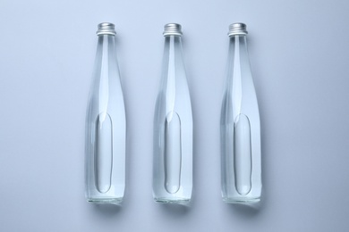 Glass bottles with water on white background, flat lay