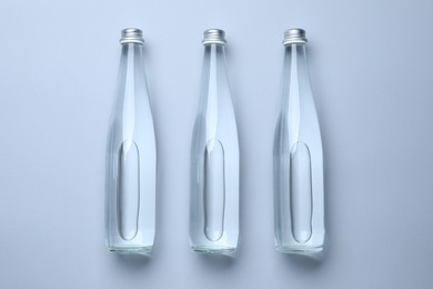 Photo of Glass bottles with water on white background, flat lay