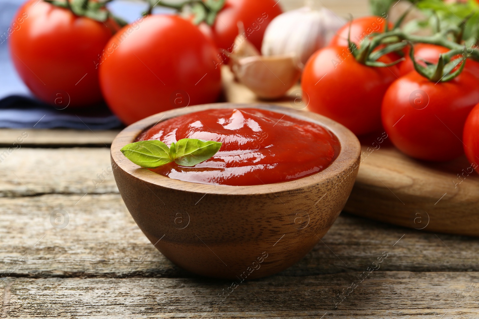 Photo of Tasty ketchup, fresh tomatoes, basil and spices on wooden table