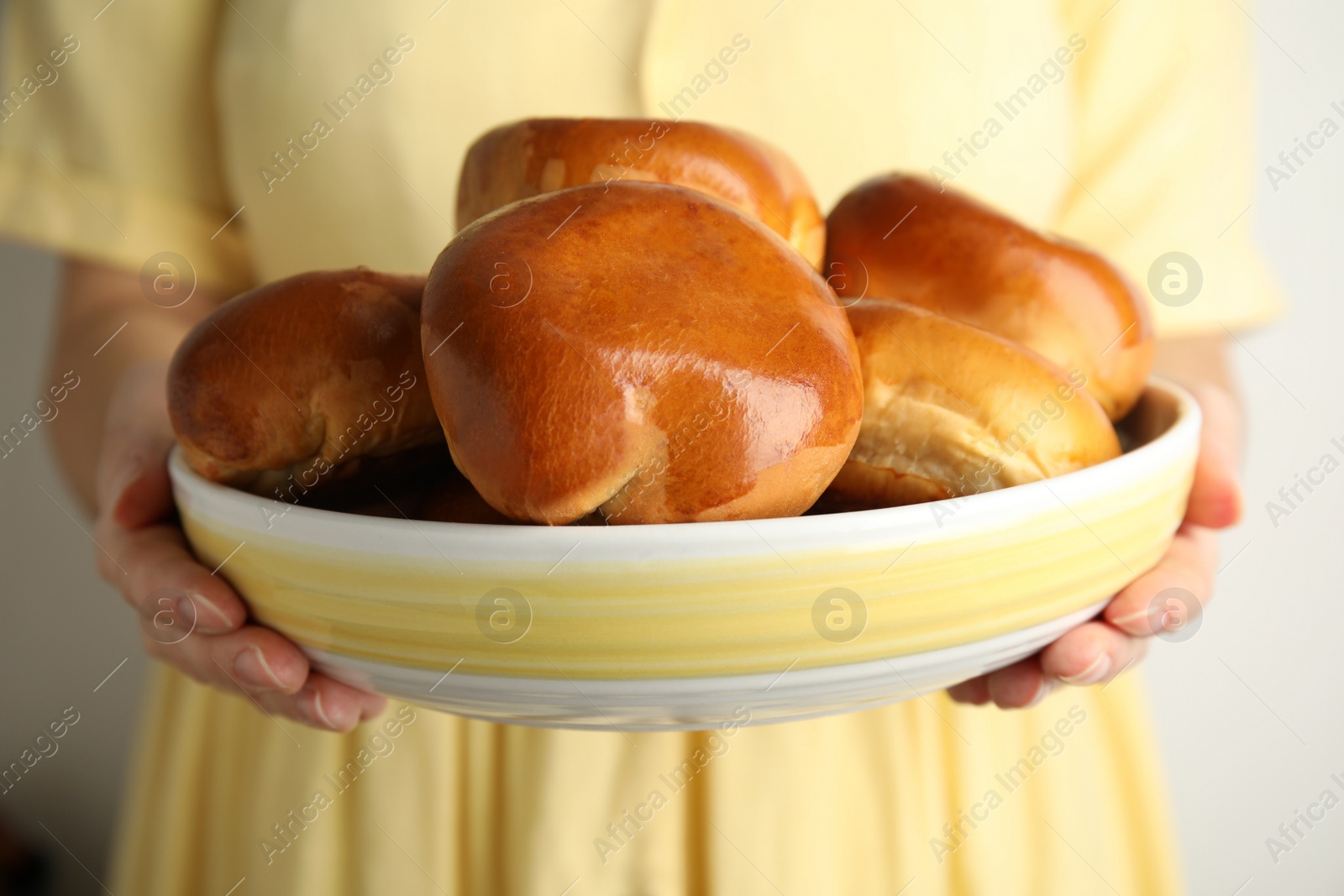 Photo of Woman holding bowl with delicious baked pirozhki on grey background, closeup