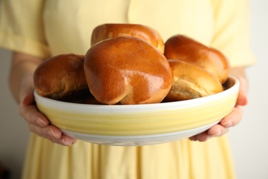 Photo of Woman holding bowl with delicious baked pirozhki on grey background, closeup