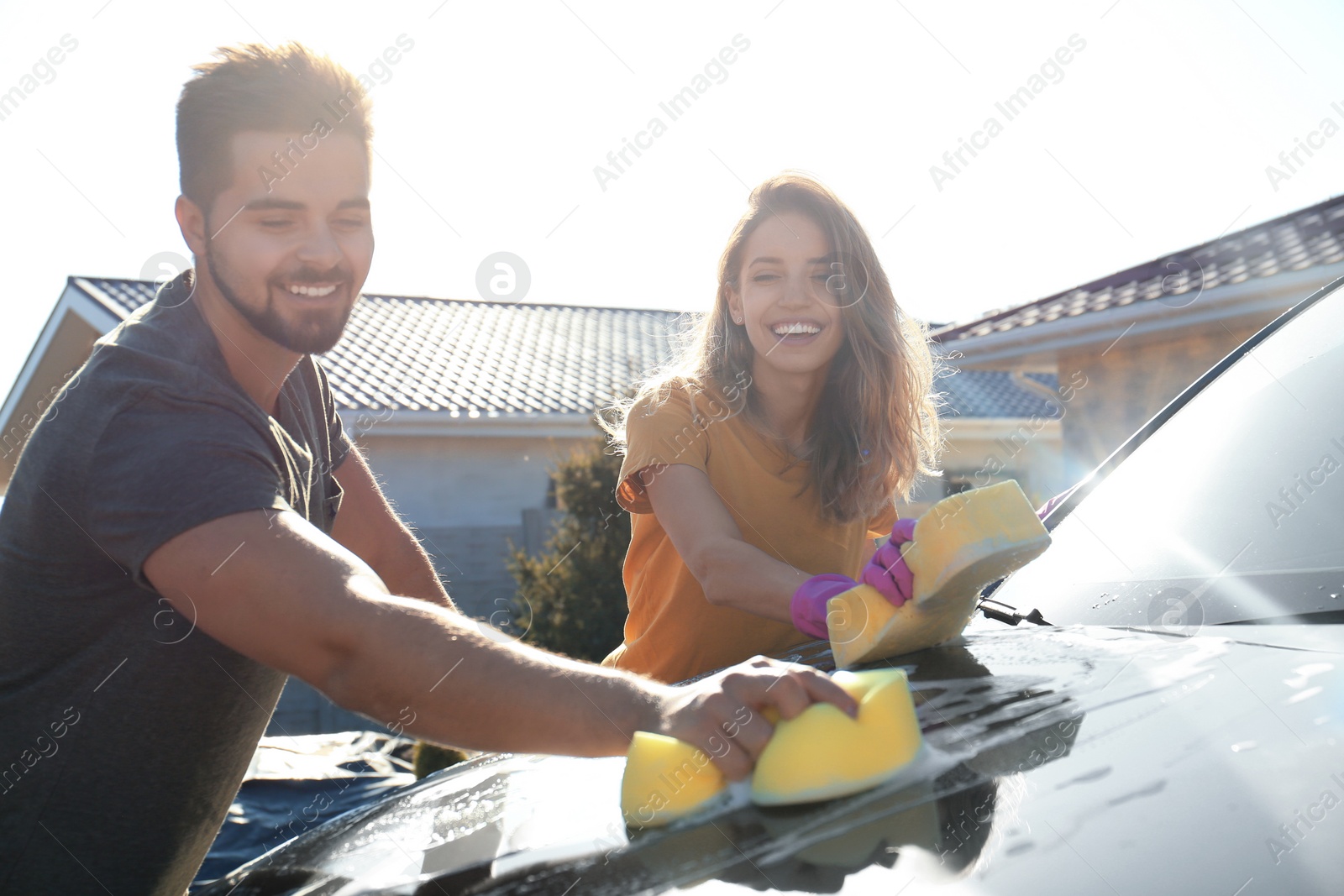 Photo of Happy young couple washing car at backyard on sunny day