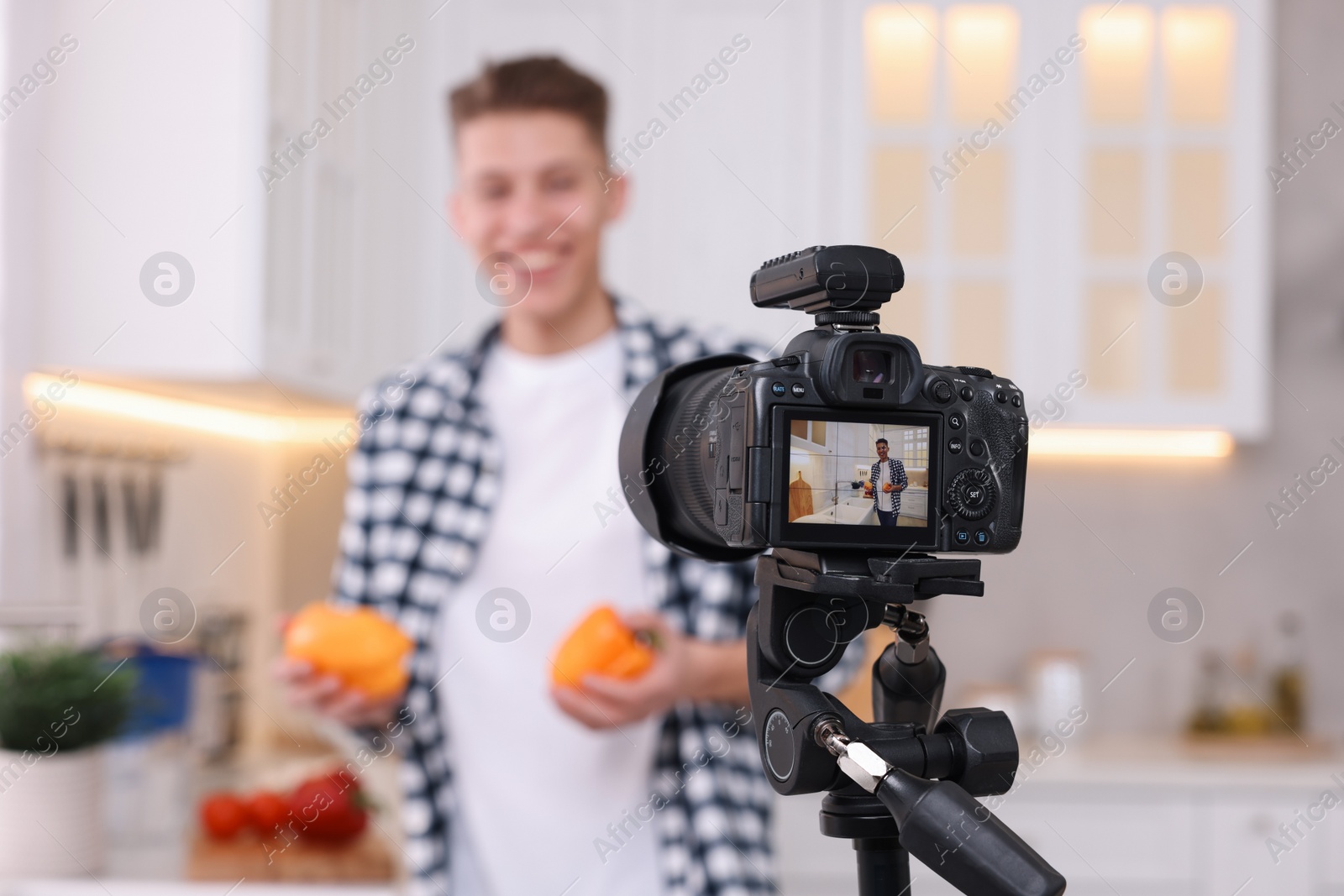 Photo of Food blogger recording video in kitchen, focus on camera