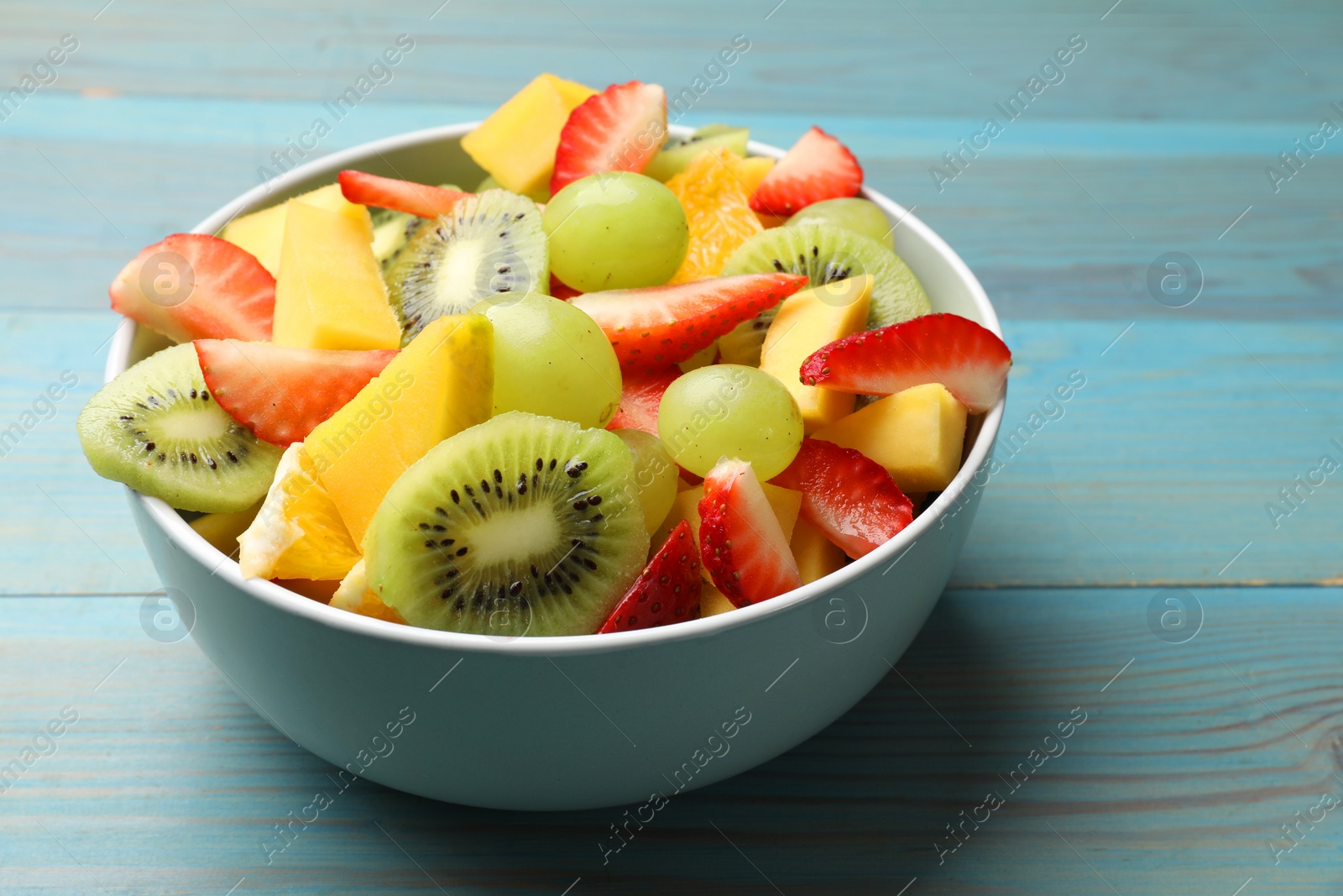 Photo of Tasty fruit salad in bowl on light blue wooden table, closeup