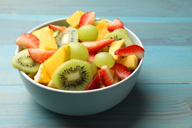 Tasty fruit salad in bowl on light blue wooden table, closeup