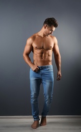 Photo of Shirtless young man in stylish jeans near grey wall