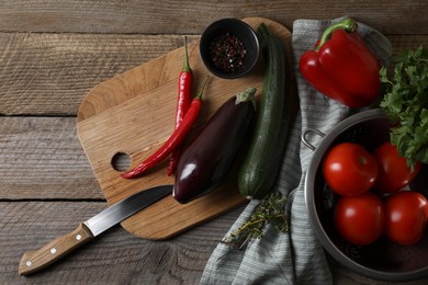 Photo of Cooking ratatouille. Vegetables, peppercorns, herbs and knife on wooden table, flat lay