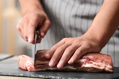 Man cutting fresh raw meat on table in kitchen, closeup