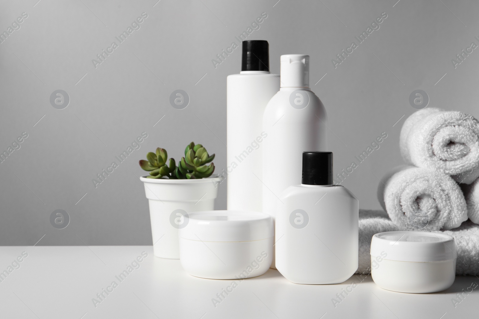 Photo of Different bath accessories, towels and houseplant on white table against grey background. Space for text