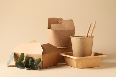 Photo of Eco friendly food packaging. Paper containers, tableware and eucalyptus branch on beige background