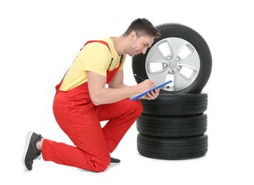 Photo of Young auto mechanic with clipboard and car tires on white background