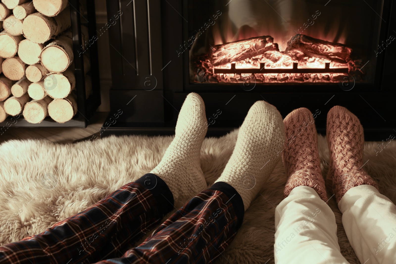 Photo of Couple in knitted socks near fireplace at home, closeup of legs