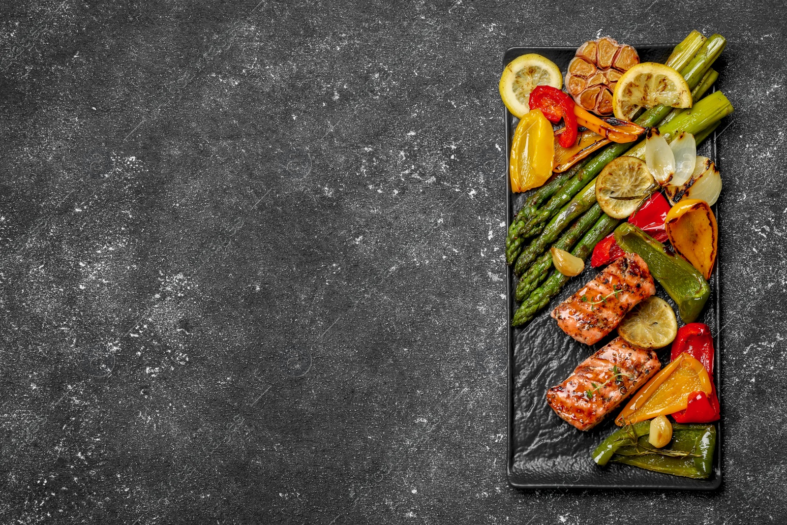 Photo of Tasty grilled salmon with lemon and vegetables on black table, top view. Space for text