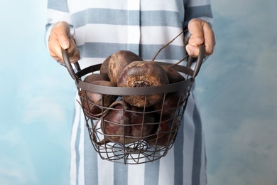 Photo of Woman holding metal basket with beets on light background