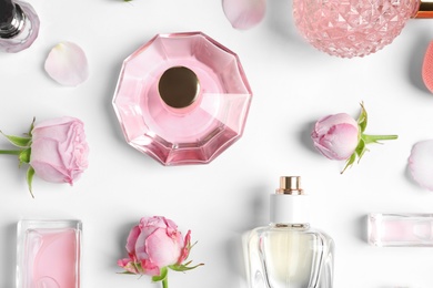 Different perfume bottles and flowers on white background, top view