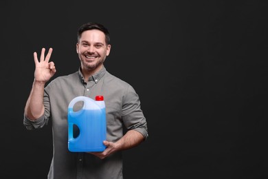 Man holding canister with blue liquid and showing OK gesture on black background, space for text