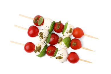 Photo of Caprese skewers with tomatoes, mozzarella balls, basil and pesto sauce on white background, top view