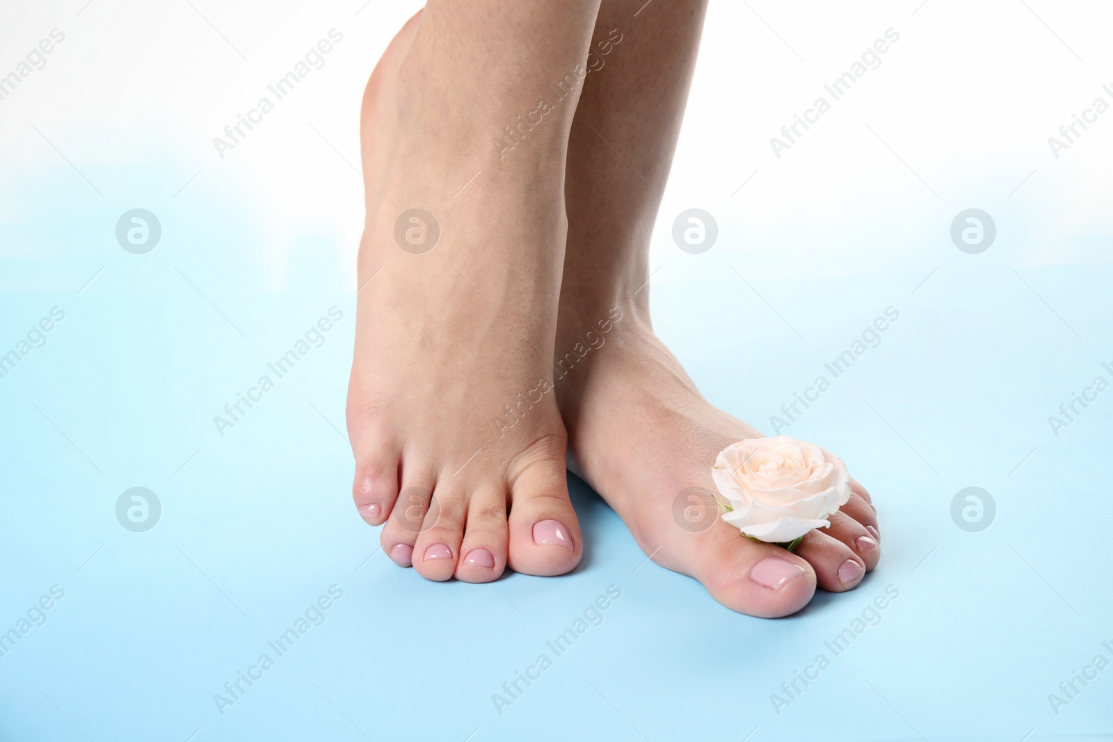 Photo of Woman with smooth feet  and flower on color background, closeup. Spa treatment