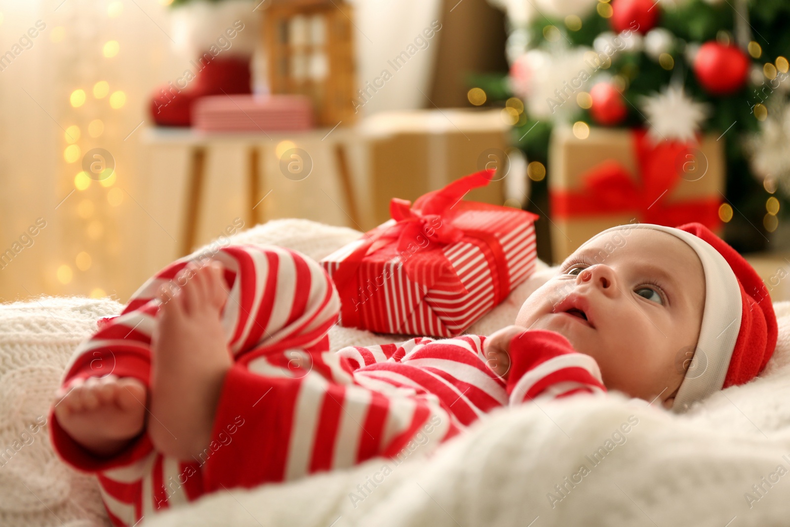 Photo of Cute little baby wearing Santa hat on blanket in room decorated for Christmas