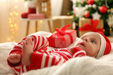 Cute little baby wearing Santa hat on blanket in room decorated for Christmas