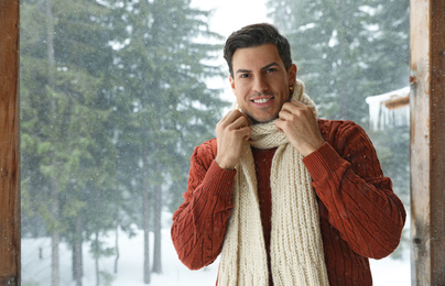 Photo of Handsome man wearing warm sweater and scarf outdoors on snowy day. Winter season