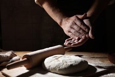 Photo of Man sprinkling flour over dough at wooden table, closeup