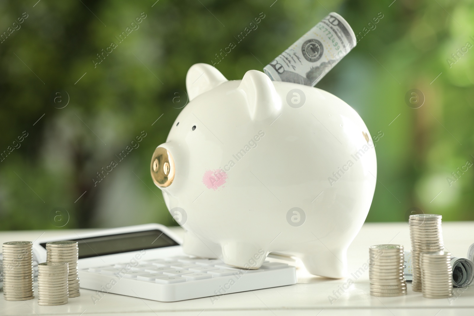 Photo of Financial savings. Piggy bank with dollar banknotes, stacked coins and calculator on white wooden table outdoors