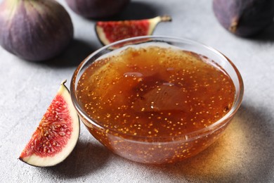 Glass bowl of tasty sweet jam and fresh figs on light table, closeup