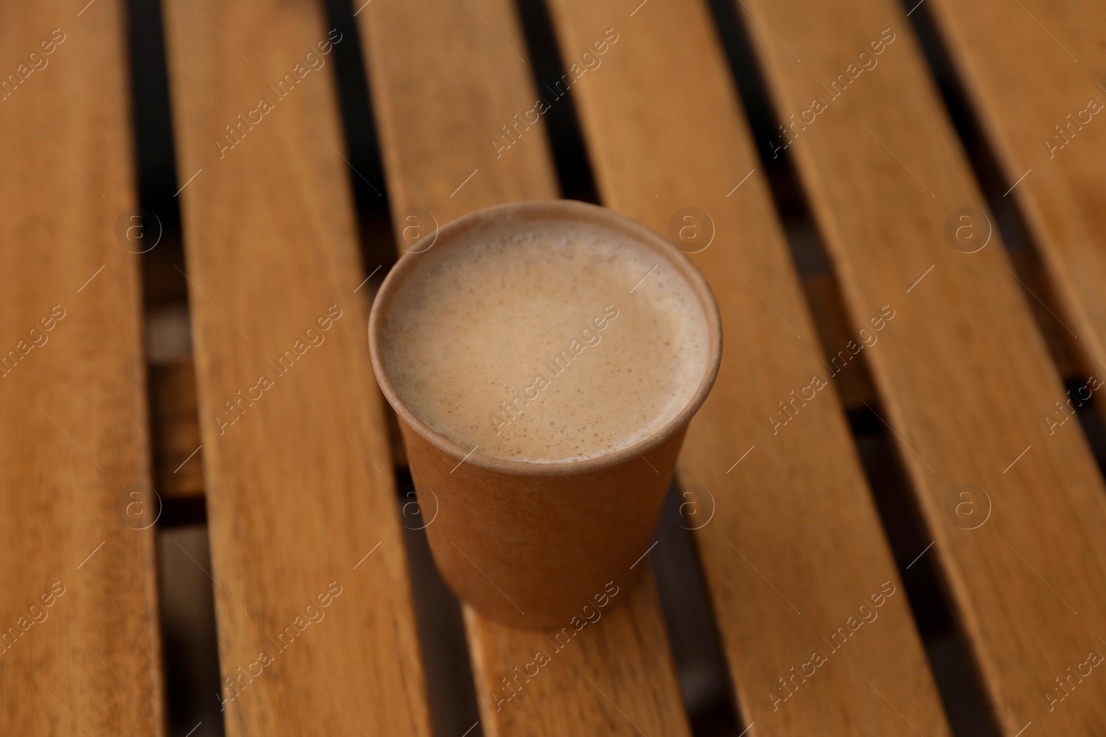 Photo of Takeaway paper cup with coffee on wooden table