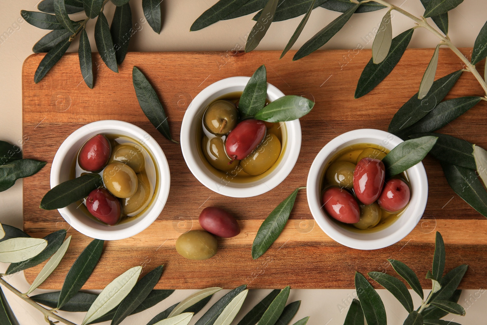 Photo of Bowls with different ripe olives and leaves on beige background, flat lay