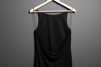 Photo of Beautiful black women's party dress on hanger near grey wall. Stylish trendy clothes for high school prom