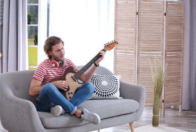 Photo of Young man with headphones playing electric guitar in living room. Space for text