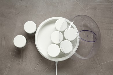 Modern yogurt maker with jars on grey table, flat lay