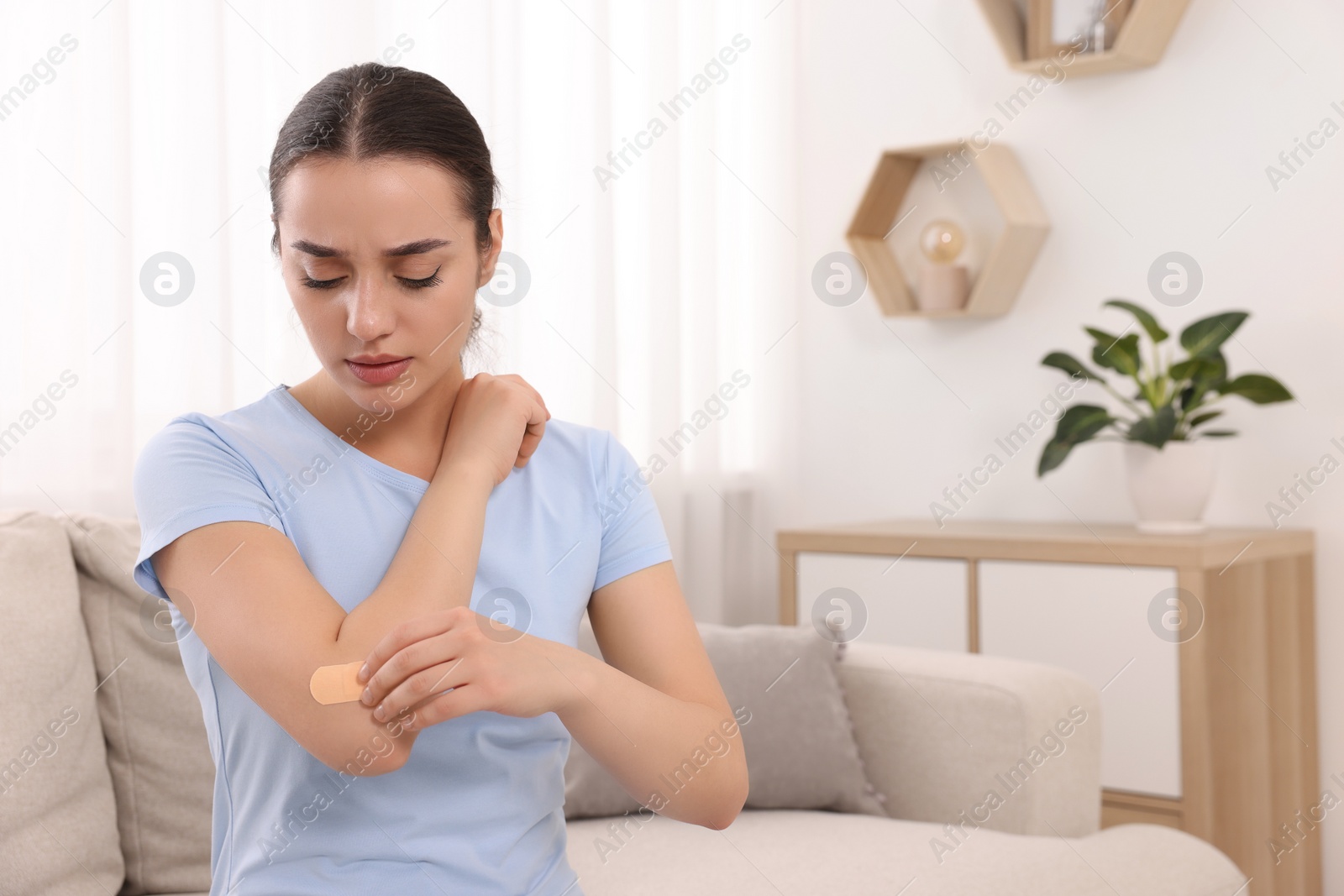 Photo of Woman putting sticking plaster onto elbow at home