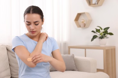 Photo of Woman putting sticking plaster onto elbow at home