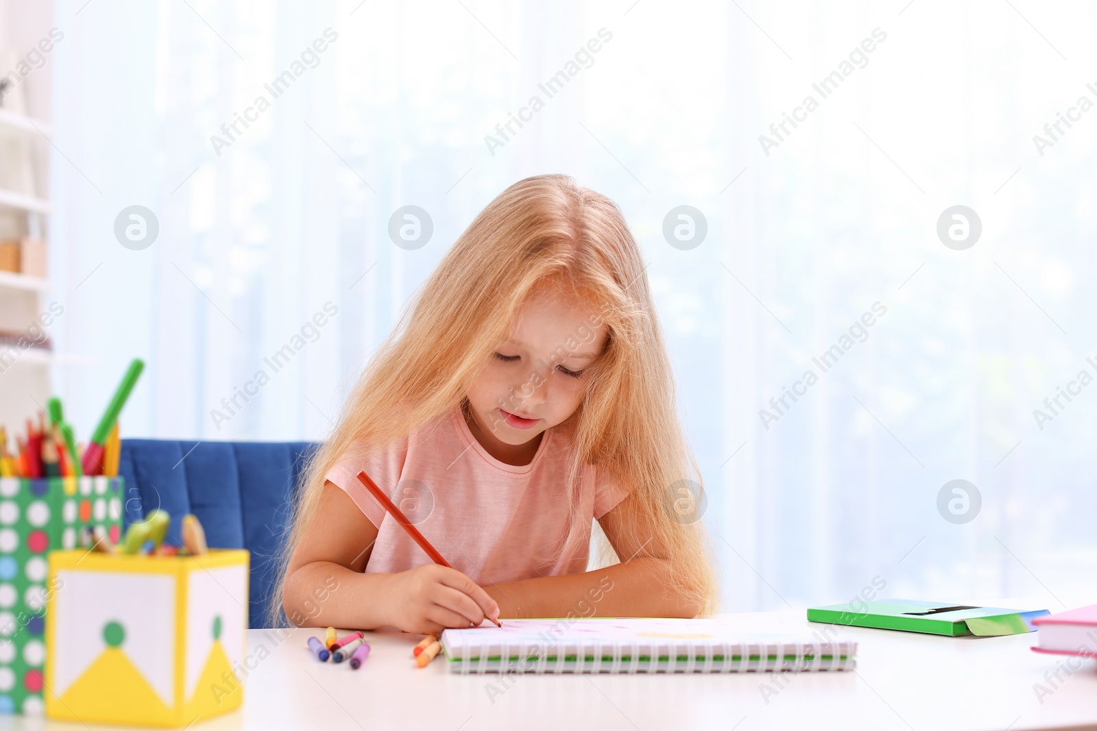 Photo of Cute little girl drawing at table in room