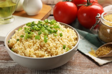 Photo of Delicious bulgur with green onion on wooden table, closeup