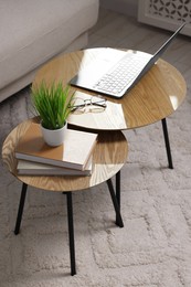 Photo of Potted artificial plant, laptop and books on wooden nesting tables indoors, above view