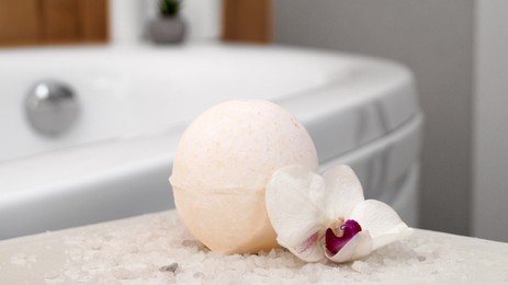 Photo of Bath bomb with orchid and sea salt on table in bathroom