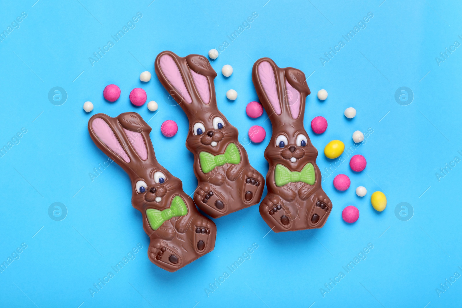 Photo of Chocolate Easter bunnies, halves of egg and candies on light blue background, flat lay