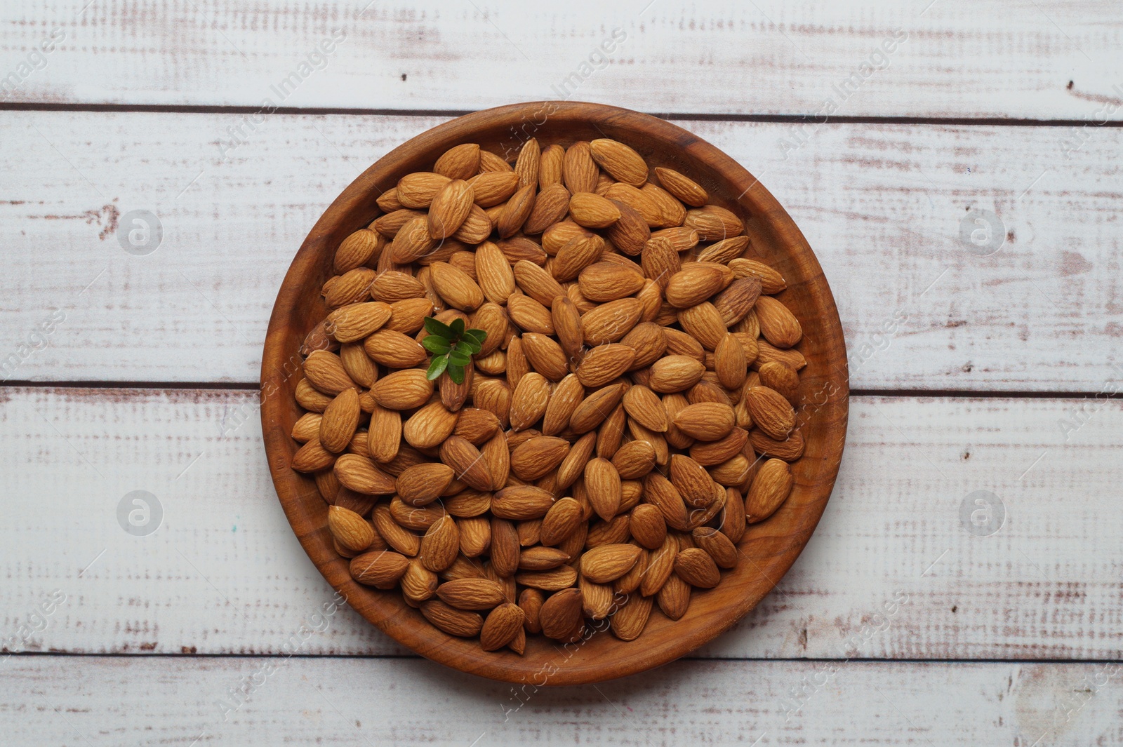 Photo of Plate with tasty almonds on white wooden table, top view