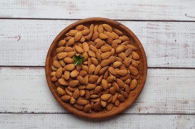 Plate with tasty almonds on white wooden table, top view